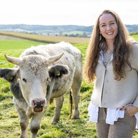 Verena Krimbacher steht auf der Kuhweide, neben ihr eine Kuh.