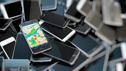 Ein angeschaltetes Smartphone liegt auf einem Berg kaputter Smartphones