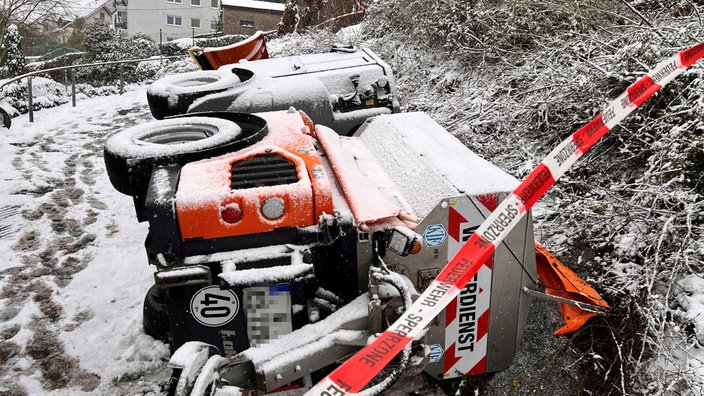 Ein Streuwagen liegt seitlich neben einem Abhang umringt von Absperrband