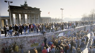 Menschenmassen auf und vor der Berliner Mauer am Brandenburger Tor während des Mauerfalls