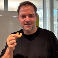 Martin Rütter in einem schwarzem T-Shirt hält ein Vanillekipferl hoch. 
