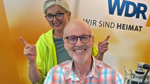 Peter Wohlleben mit Heike Knispel im WDR 4 Studio: Peter Wohlleben trägt ein kariertes Hemd und sitzt am Mikro, Heike Knispel steht in einer neongrünen Jacke hinter ihm. Im Hintergrund sieht man den WDR 4 Schriftzug an der Wand.