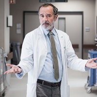 Eine Szene aus der Serie "Doktor Ballouz": Dr. Amin Ballouz (Merab Ninidze) im Arztkittel mit ausgestreckten Armen im Gang eines Krankenhauses