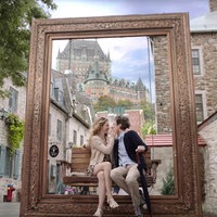 Szene aus dem Film "French Girl": Sophie, gespielt von Evelyne Brochu, und Gordon, gespielt von Zach Braff, sitzen auf einer Bank, die als Fotospot vor einem übergroßen Bilderrahmen aufgestellt ist. Sie nähern sich zum Kuss, ihre Hand ist an seiner Wange.