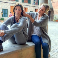 Filmszene aus dem Film "Insel der Zitronenblüten": Marina (gespielt von Elia Galera) und Anna (gespielt von Eva Martin) sitzen auf einem Mauervorsprung. Anna flechtet Marinas Haare. 
