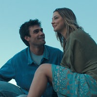 Eine Szene des Films "Liebe findet uns": Die Schauspieler KJ Apa und Madelyn Cline sitzen lächelnd nebeneinander vor einem blauen Himmel