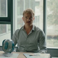 Szene aus dem Film " Pfau – Bin ich echt?": Matthias, gespielt von Albrecht Schuch sitzt an einem Schreibtisch. Hinter ihm befindet sich eine Fensterfront. 