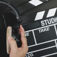 Eine Filmklappe liegt auf einem schwarzen Untergrund, davor wird ein Paar Kopfhörer gehalten.