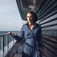 Eine Szene aus dem Film "The Woman in Cabin 10": Journalistin Laura "Lo" Blacklock, gespielt von Keira Knightley, steht an der Reling eines Kreuzfahrtschiffes. Sie trägt ein blaues Businesskleid und schaut ernst in die Ferne. 