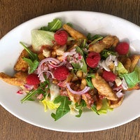 Blattsalat mit Hähnchenbruststreifen auf einem Teller, darauf ein paar Himbeeren