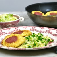 Ein angerichteter Teller mit Klitschkes, daneben Lauchgemüse in Sauce. Im Hintergrund sieht man eine Schüssel mit dem restlichen Lauchgemüse und die Pfanne mit den restlichen Klitschkes. 