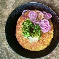 Schweizer Rösti in einer Pfanne mit Zwiebelringen und Feldsalat