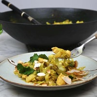 Spitzkohl und Hähnchen in Curry-Kokos-Sauce ist auf einem Teller angerichtet, im Hintergrund stehen ein Glas mit frischem Koriander und das restliche Curry in einer Wok-Pfanne