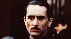 Robert de Niro in "Der Pate II", Mann mit schwarz zurückgekämmten Haaren und Schnurrbart schaut düster