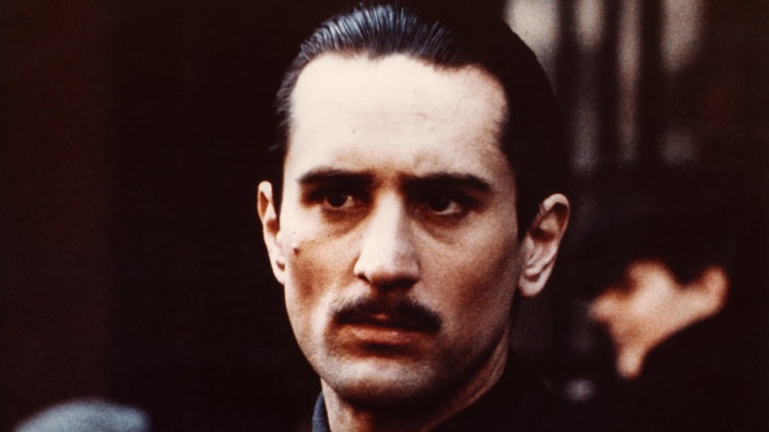 Robert de Niro in "Der Pate II", Mann mit schwarz zurückgekämmten Haaren und Schnurrbart schaut düster