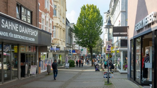 In einer Fußgängerzone mi verschiedenen Läden sind Menschen unterwegs
