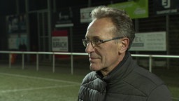 Ein grauhaariger Mann steht auf einem Fußballplatz