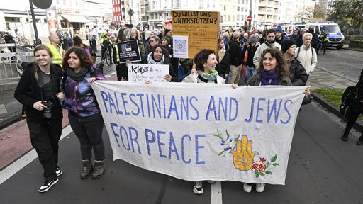 Eine Gruppe an Demonstranten läuft über die Straße mit einem Banner, auf dem steht "Palestinians and Jews for Peace"