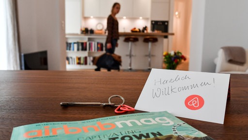 Ein Schlüssel mit einem Airbnb-Anhäger, ein Airbnbmag-Magazin und eine Herzlich-Willkommen-Karte liegen in der Wohnung eines Airbnb-Gastgebers