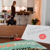  Ein Schlüssel mit einem Airbnb-Anhäger, ein Airbnbmag-Magazin und eine Herzlich-Willkommen-Karte liegen in der Wohnung eines Airbnb-Gastgebers