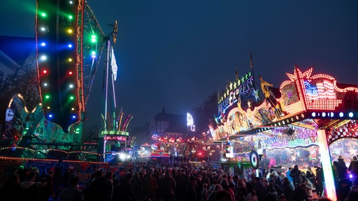 Menschen laufen zwischen Fahrgeschäften über die Allerheiligenkirmes in Soest