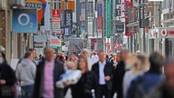 Viele Menschen bewegen sich auf einer Einkaufsstraße mit vielen Geschäften in Köln