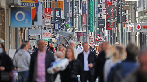 Viele Menschen bewegen sich auf einer Einkaufsstraße mit vielen Geschäften in Köln