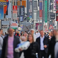 Viele Menschen bewegen sich auf einer Einkaufsstraße mit vielen Geschäften in Köln