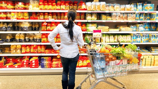 Eine Frau steh vor einem Supermarkt-Regal mit Lebensmitteln in Plastik eingeschlagen