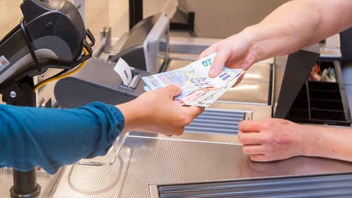 Eine Frau lässt sich an einer Kasse in einem Supermarkt Bargeld auszahlen