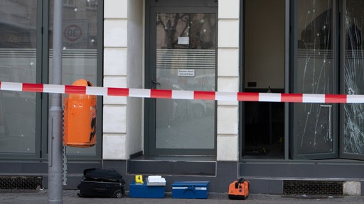 Vor einem abgesperrten Lokal liegen Koffer der Polizei. Die Scheiben des Lokals sind beschädigt.