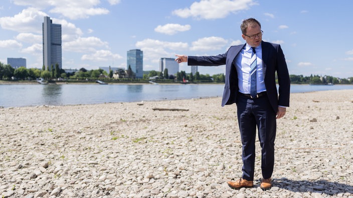 Bundesumweltminister Carsten Schneider steht bei Niedrigwasser am Rhein bei Bonn