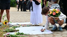 Ein Mann schreibt eine Trauerbekundung auf ein Papier und legt Blumen nieder nahe dem Angriffsort in Berlin.