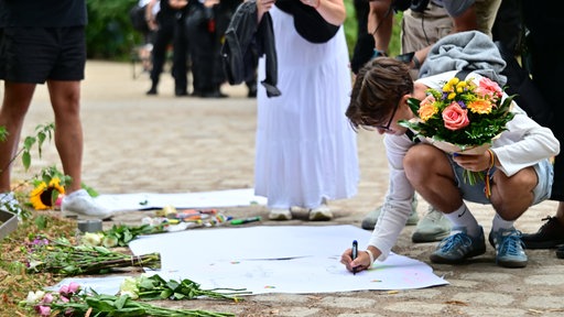 Ein Mann schreibt eine Trauerbekundung auf ein Papier und legt Blumen nieder nahe dem Angriffsort in Berlin.