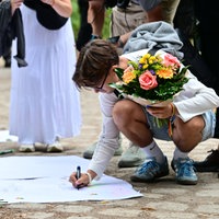 Ein Mann schreibt eine Trauerbekundung auf ein Papier und legt Blumen nieder nahe dem Angriffsort in Berlin.