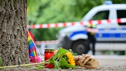 Eine Regenbogenflagge, Blumen und Kerzen stehen vor einem Baum nahe dem Bereich, wo ein Fahrzeug einen Baum gerammt hatte nach dem Anschlag in Berlin