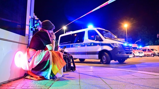 Eine in eine Pride-Fahne gehüllte Person hockt neben einem Polizeifahrzeug nach dem Abbruch des Berliner Christopher Street Days