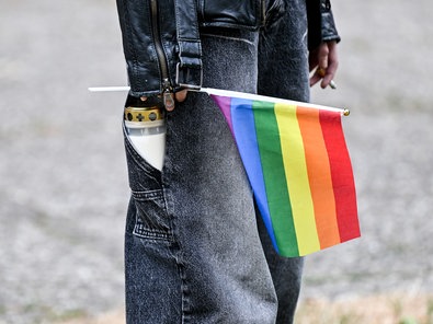 Eine Person mit einer Treuerkerze in der Hosentasche hält eine Pride-Flagge in der Hand