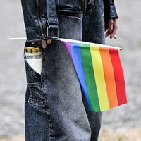 Eine Person mit einer Treuerkerze in der Hosentasche hält eine Pride-Flagge in der Hand