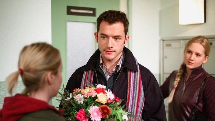 Alex (Joris Gratwohl) kommt mit Blümchen und einem schlechten Gewissen zu Lisa (Sontje Peplow, rechts) – und wird auf halbem Wege von Valerie (Nadine Spruß) abgefangen.