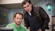 Alex und Murat schauen auf einen Bildschirm im Reisebüro