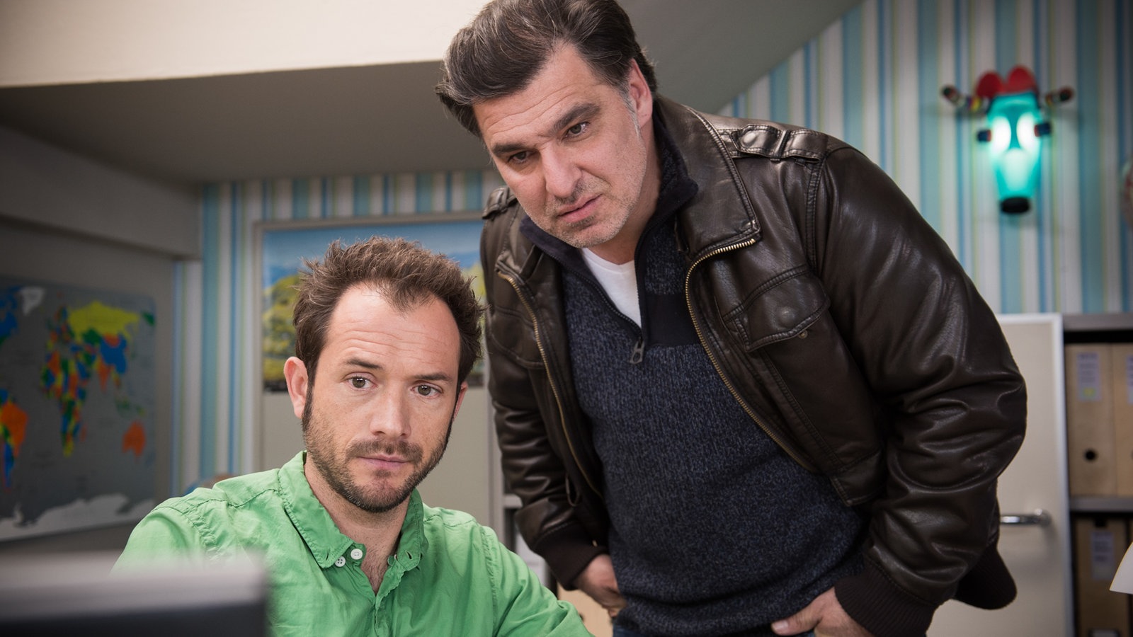 Alex und Murat schauen auf einen Bildschirm im Reisebüro