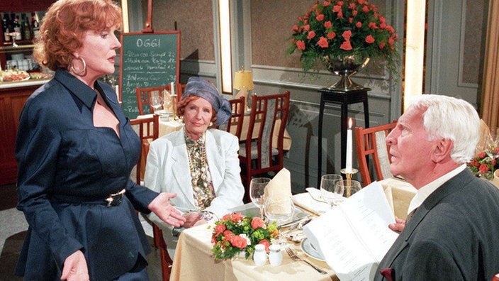 Amélie (Anna Teluren) und Priesnitz (Carlos Werner) lassen sich von Isolde (Marianne Rogée, links) bei der Menuwahl beraten.