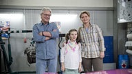 Andy, Gabi und Antonia stehen in der Werkstatt vor dem Camaro