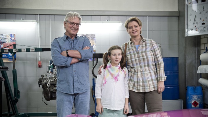 Andy, Gabi und Antonia stehen in der Werkstatt vor dem Camaro