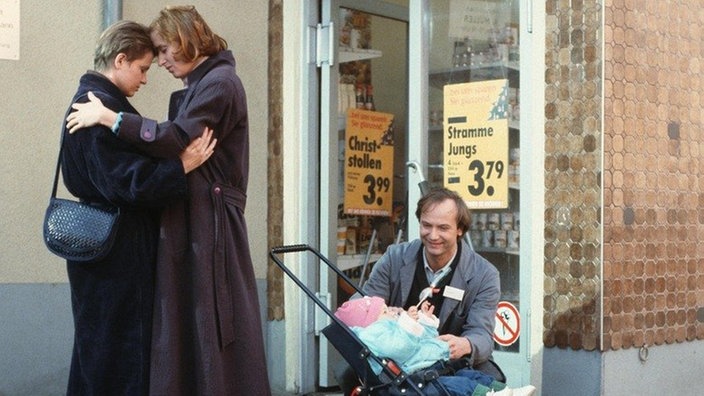 Anna (Irene Fischer) und Gabi (Andrea Spatzek, links) suchen Trost bei einander. Friedhelm (Arnfried Lerche) nutzt die Gelegenheit und spielt mit Sarah.