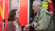 Anna und Hans stehen vor einem Krankenwagen und reden