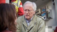 Anna und Hans stehen vor einem Krankenwagen und reden