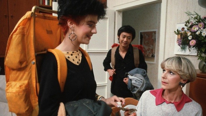 Beate (Susanne Gannott, links) und Gung (Amorn Surangkanjanajai) wollen einen Wochenendausflug an den Bodensee machen. Elisabeth (Dagmar Hessenland) sponsort den Kurztripp.