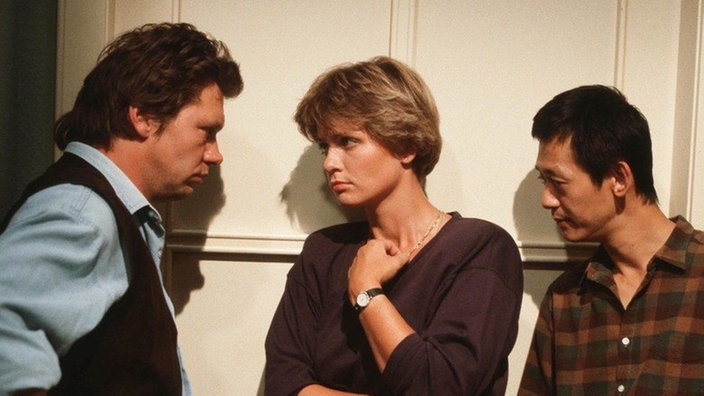 Benno (Bernd Tauber, links), Gabi (Andrea Spatzek) und Gung (Amorn Surangkanjanajai) lauschen besorgt an Annas Tür.